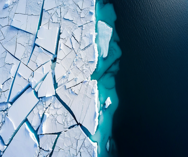 Aerial view of Antarctic sea ice showing the transition between solid white ice sheets and dark blue ocean water, with visible fracture patterns and ocean currents illustrating the complex interaction of multiple environmental forces driving ice loss
