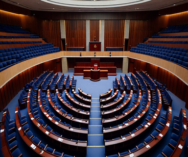 An elevated view of an empty parliamentary chamber with curved rows of seats arranged in a semicircular pattern, symbolizing the conclusion of a legislative session and the challenges of political consensus-building